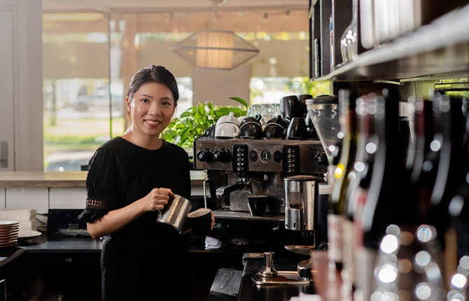 Female student standing infront of a coffee machine making coffee